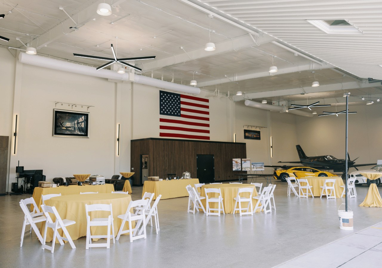 Bright hangar interior arranged with round tables and white chairs for an event